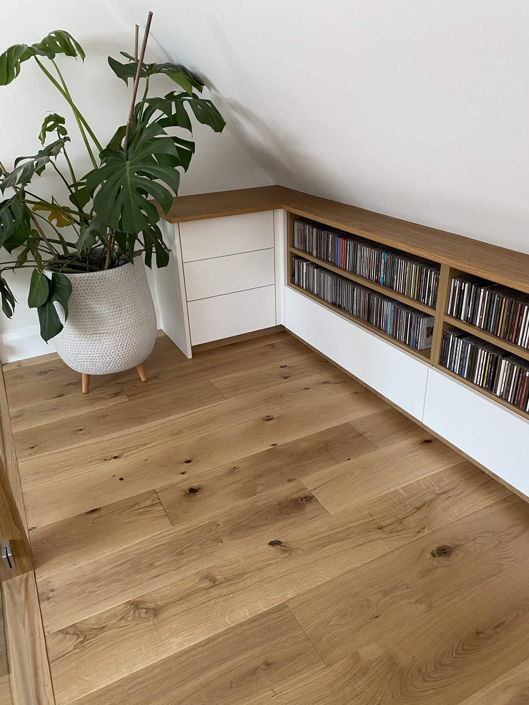 Low-level fitted storage under an eaves slope with oak-framed CD shelving and white drawers