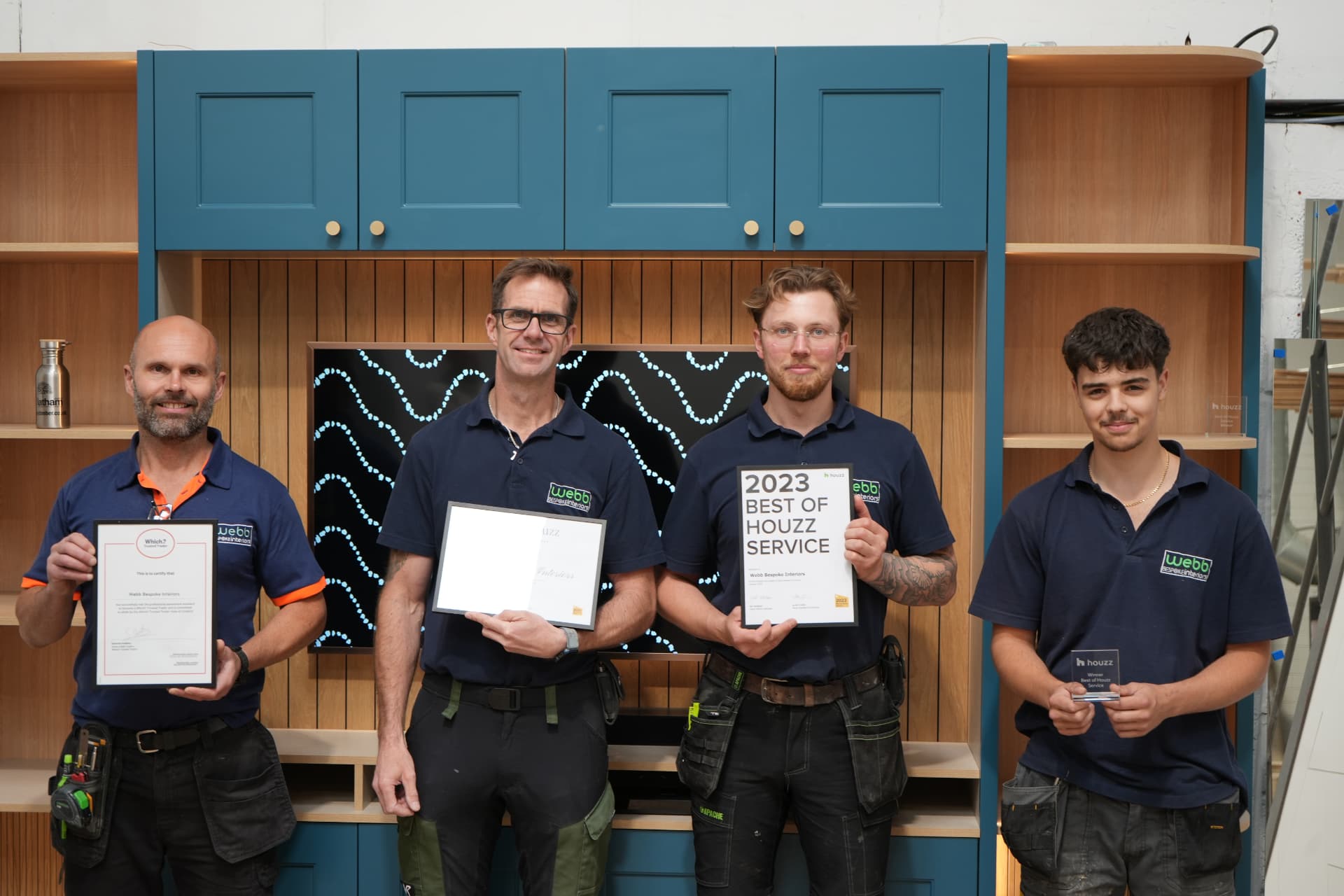 The Webb Bespoke Interiors team, four craftsmen in branded polo shirts holding their Which? Trusted Trader and Houzz awards in front of a bespoke fitted storage unit