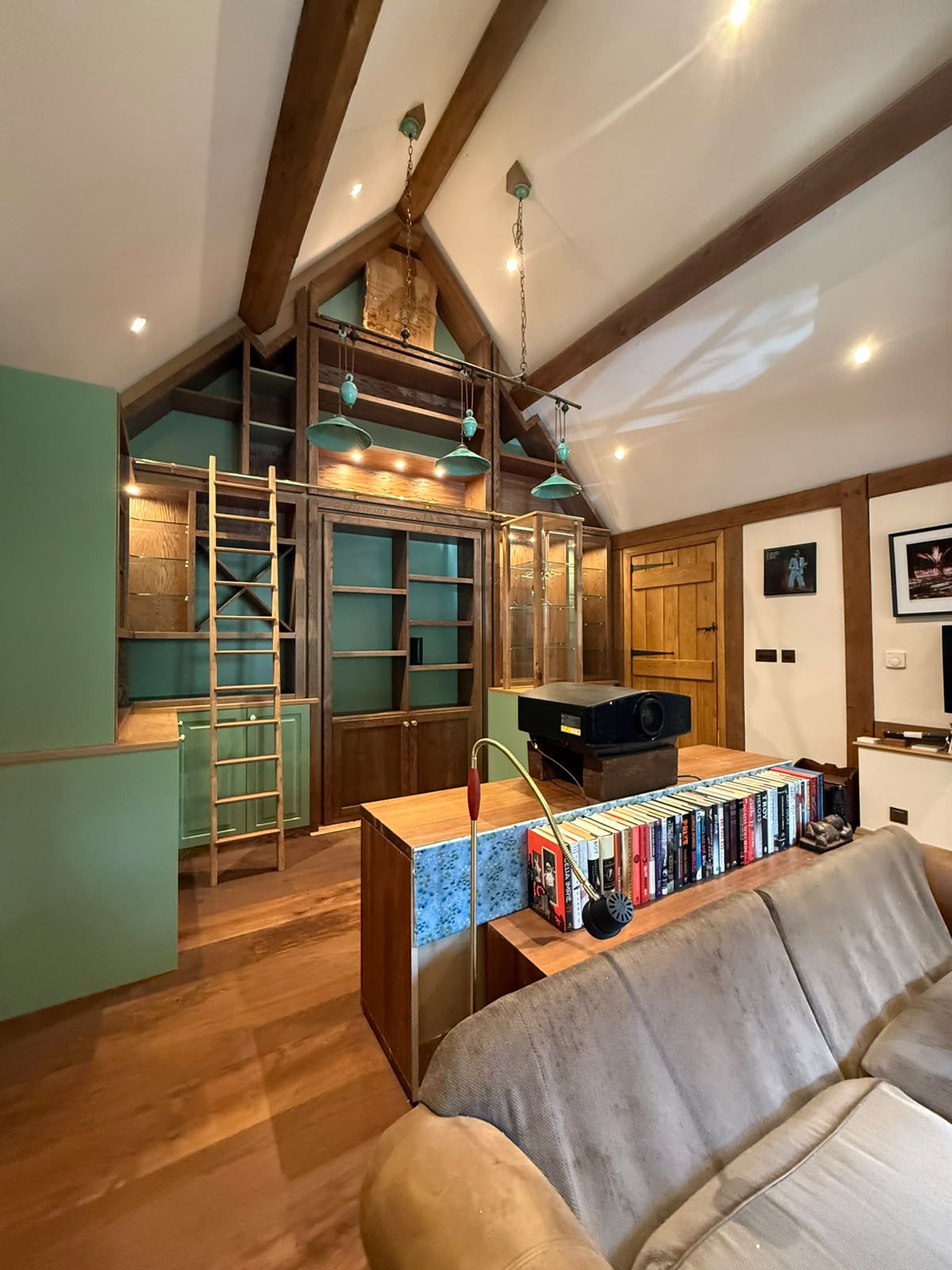 Oak library shelving and display cabinetry with ladder in a vaulted beamed room