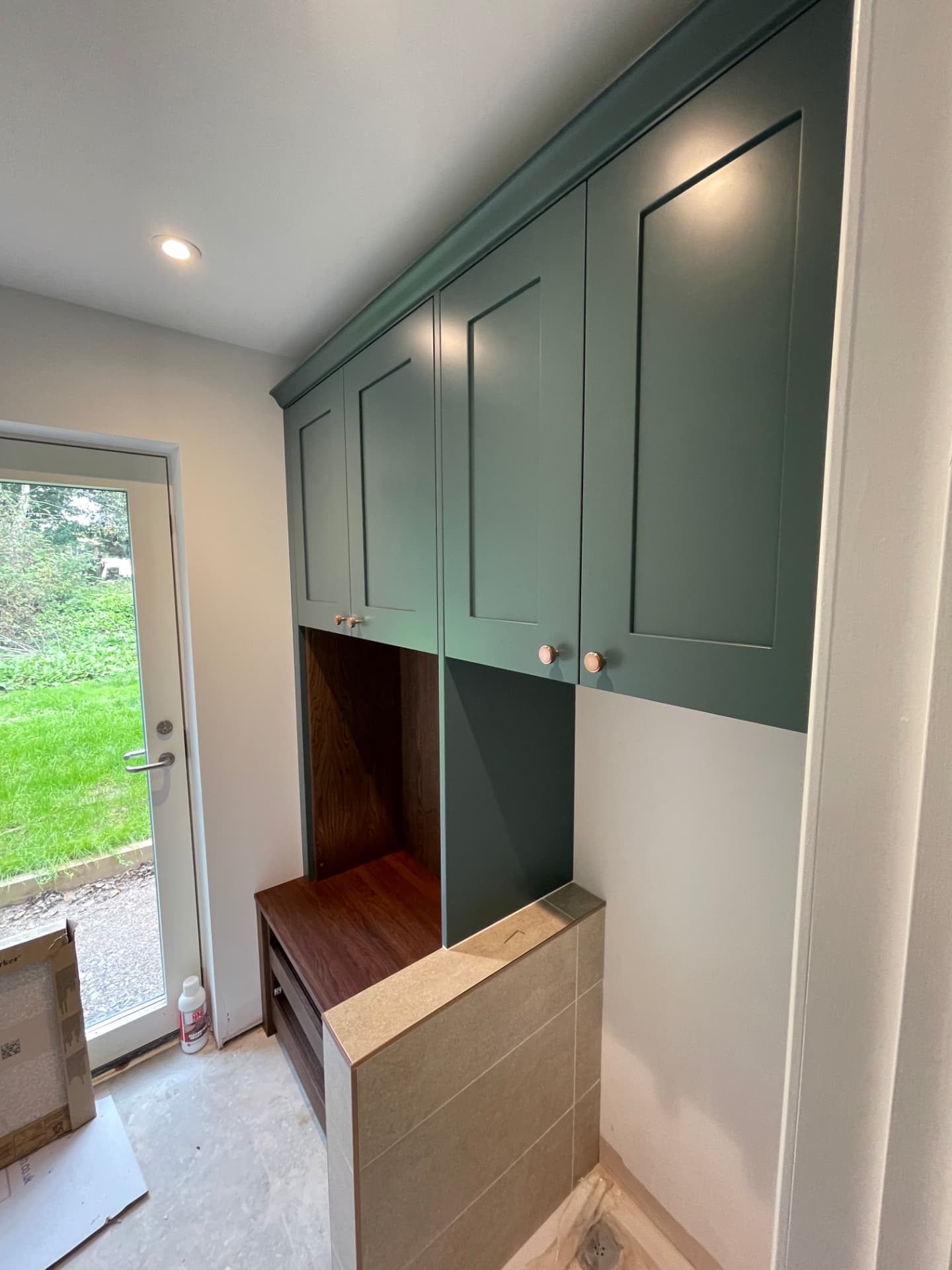 Green fitted utility and boot room cabinetry with oak bench seat and lit interiors